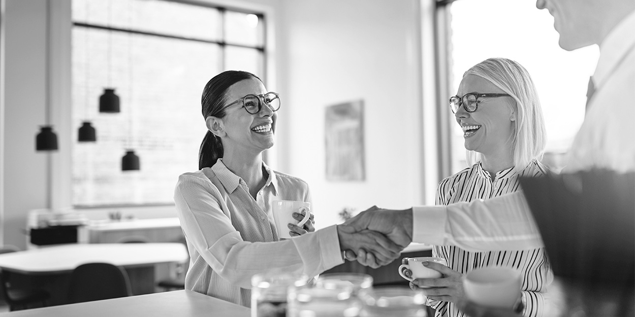 ma two business woman happy with one shaking the hand of a businessman